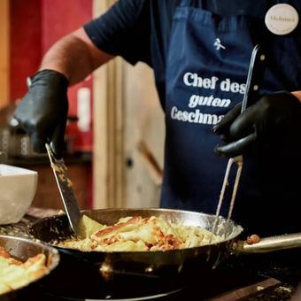 Ein Koch mit Kochschürze rührt Schupfnudeln in einer gußeisernen Bratpfanne