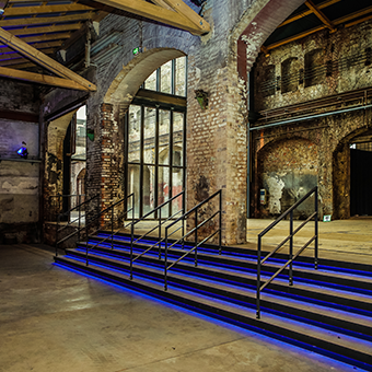 Treppe und Gang in der Kulturwerft. Viele Rundbögen, die Treppe ist blau beleuchtet
