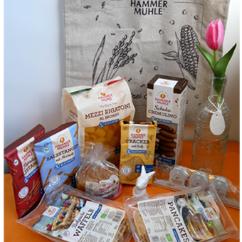 hinten hängt eine Tasche von Hammermühle, davor stehen Nudeln, Kekse, Salzstangen, Waffeln und Pancakes.