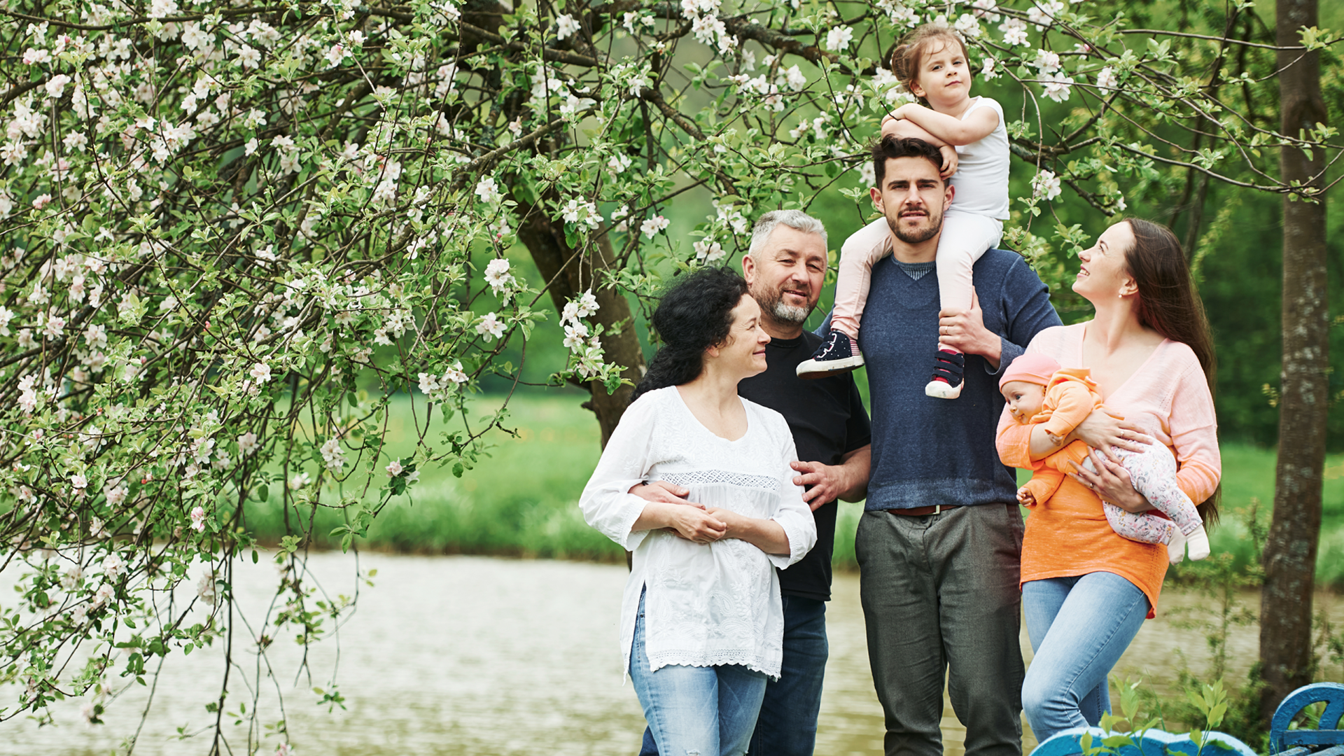 Familie mit 2 kinder und Großeltern stehen unter einem weiß blühenden Frühlingsbaum