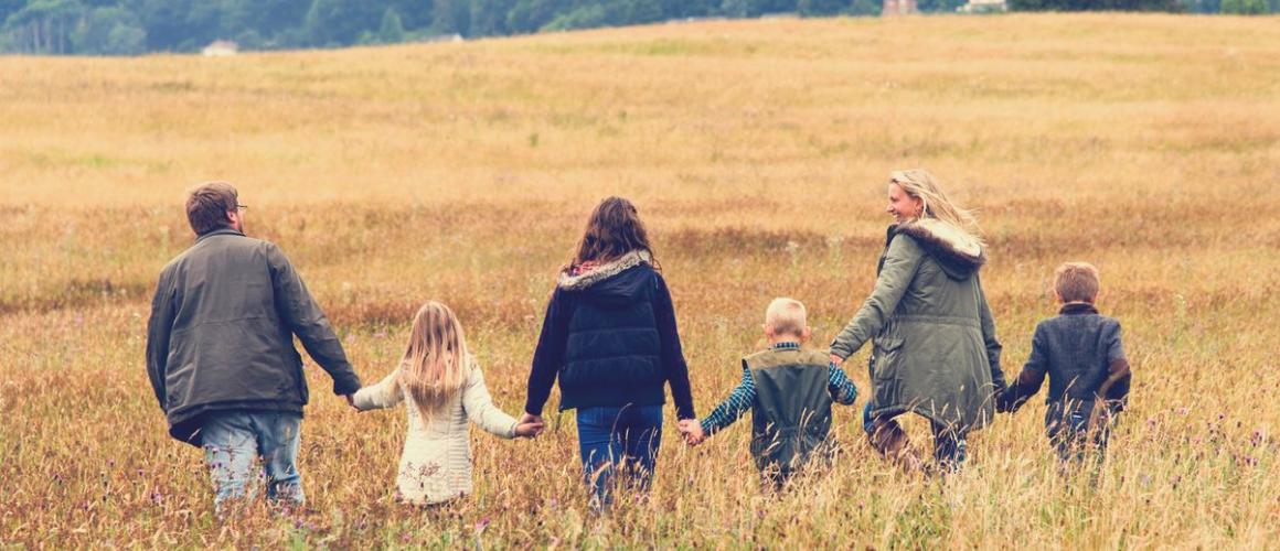 Familie mit zwei Elternteilen und vier Kindern laufen durch ein Feld