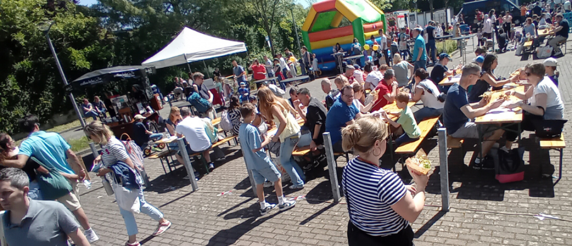 Kindererlebnistag 2025 Kindererlebnistag 2025 Außengelände mit Hüpfburg, vielen Bänken und Tischen, Essensstände und relaxten Menschen- die Sonne scheint