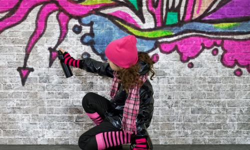 Mädchen sprüht Graffiti an eine Wand
