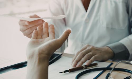 Arzt reicht dere Hand einer Patientin eine Überweisung