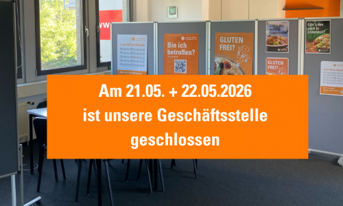 Innenaufnahme eines Besprechungsraumes der DZG mit Stellwänden und orangefarbenen Plakaten zum Thema Glutenfreiheit und Zöliakie. In der Bildmitte steht auf einem großen orangefarbenen Hinweis: „Am 21.05. + 22.05.2026 ist unsere Geschäftsstelle geschlossen.